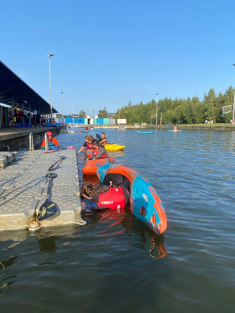 People kayaking near a dock on a sunny day with trees in the background.