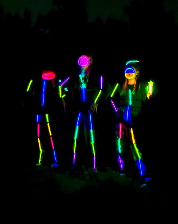 Three glow stick figures in dark forest night scene with stars above.