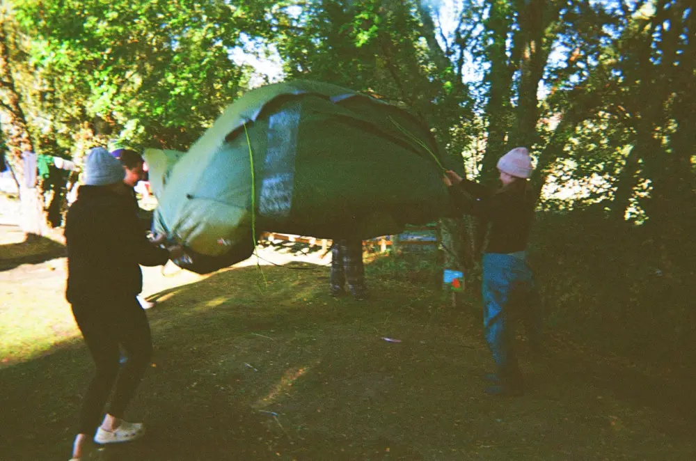 Two people setting up a green tent in a wooded area.