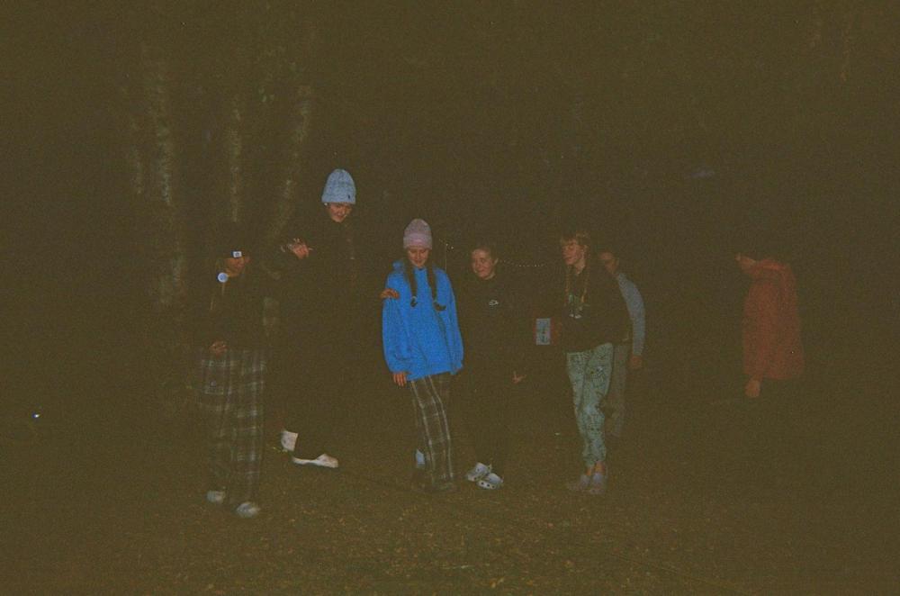 Group of people wearing warm clothes and beanies, standing outdoors at night.