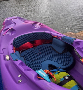 Purple kayak with blue seat and gear, docked by a calm lake.