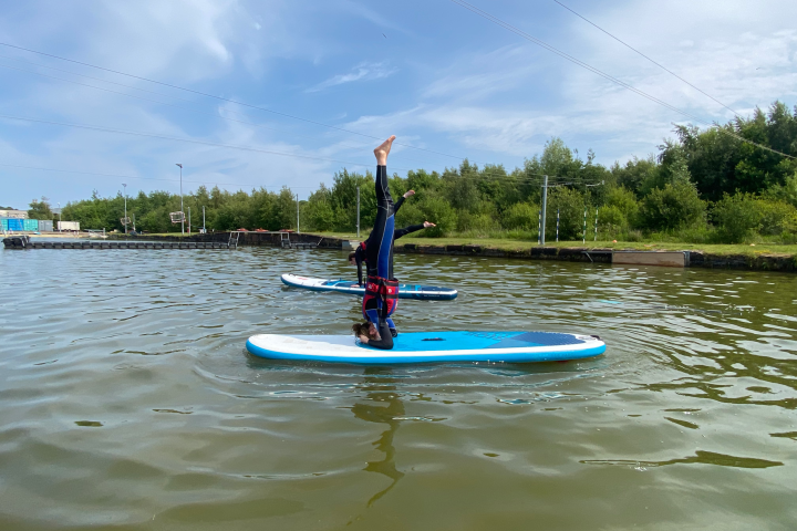 Person doing a headstand on a paddleboard in a lake.