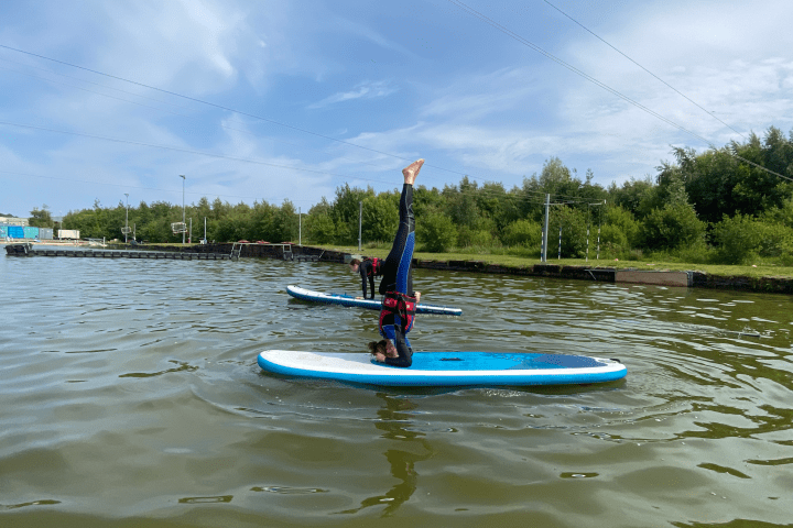 Person doing a headstand on a paddleboard in a lake.