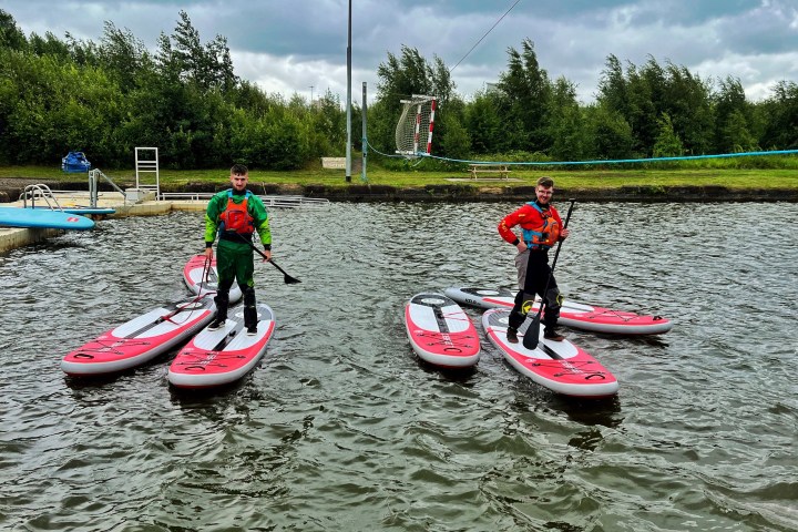 Two people paddleboarding on a lake with trees in the background.
