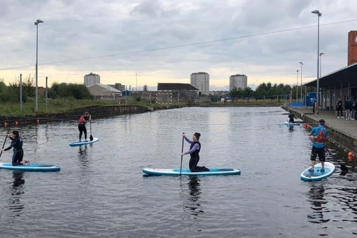 People paddleboarding on a calm canal with cloudy skies.