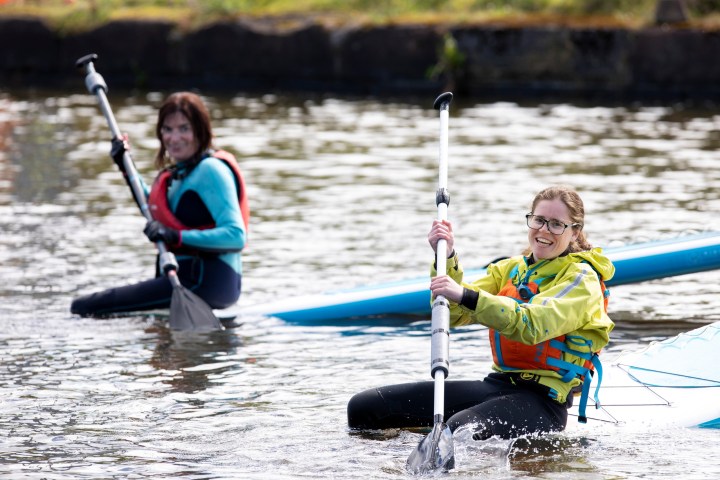Two people kayaking on a calm river, smiling and holding paddles.