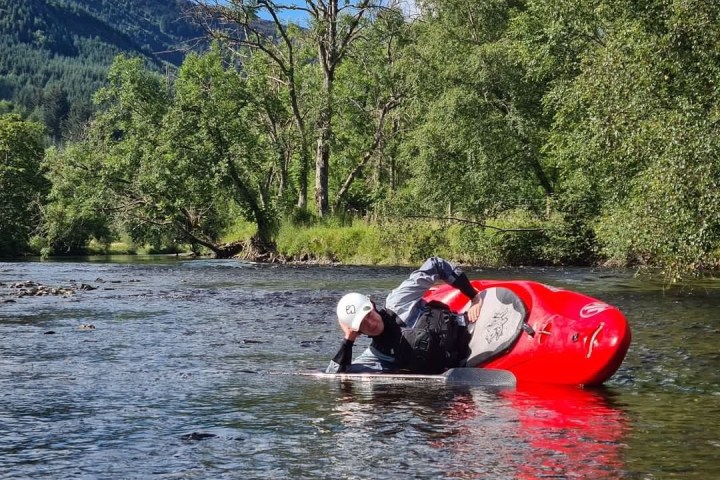 Person kayaking in a scenic river with trees and hills in the background.
