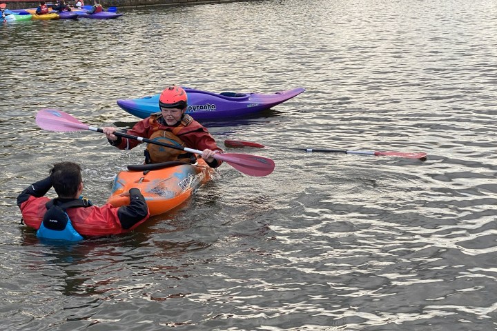 Person in kayak assists another in water near fallen paddle.