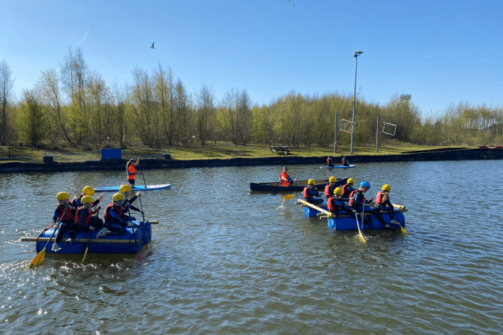 People on rafts and a kayak paddling on a lake under a clear sky.