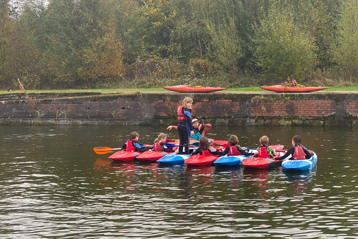 Group of people in kayaks on a river near a grassy bank.