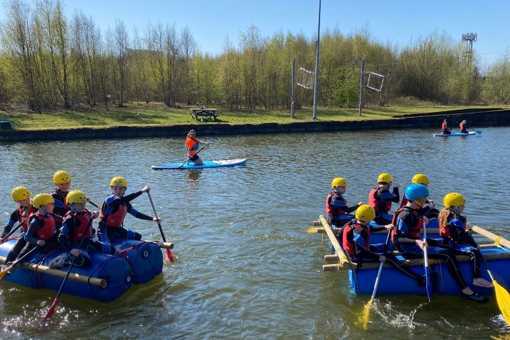 People rafting and kayaking on a sunny river with trees in the background.