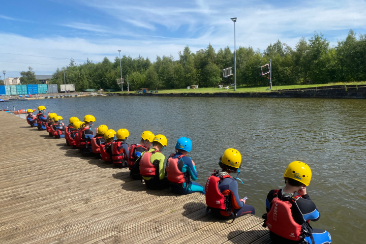 Group of people in helmets and life jackets sitting by a waterfront.
