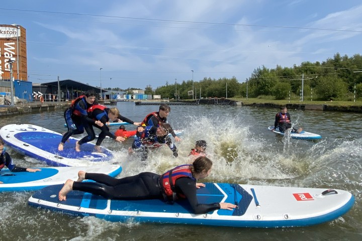 People in life vests falling off paddleboards into a canal.