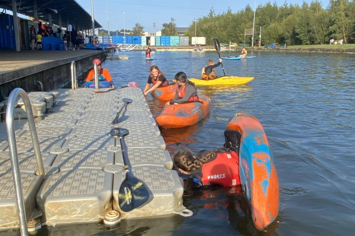 People in kayaks near a floating dock on a sunny day.