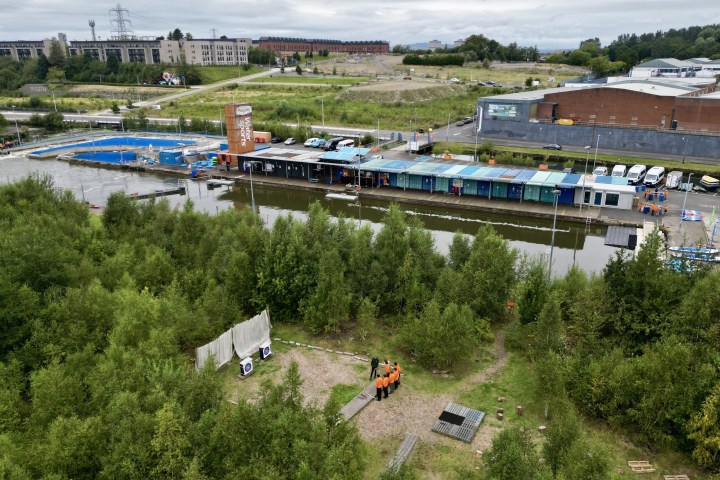 Overview of a green park area with industrial buildings and a river in the background.
