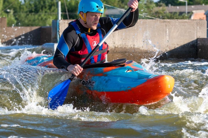 Person kayaking through white water with a blue helmet and paddle.