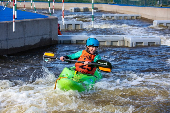 Person kayaking through whitewater with paddles, wearing helmet and life jacket.