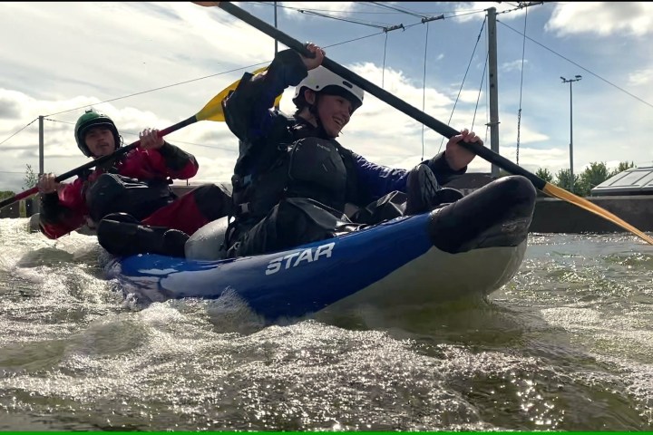 Two people kayaking in tandem on a river with safety gear.