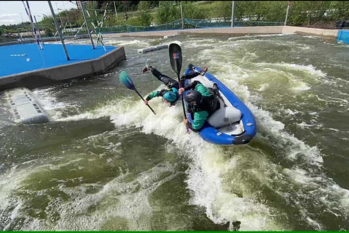 Two people in a kayak navigating whitewater rapids on a sunny day.