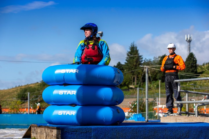 Person in blue gear with stacked blue rafts, outdoors.