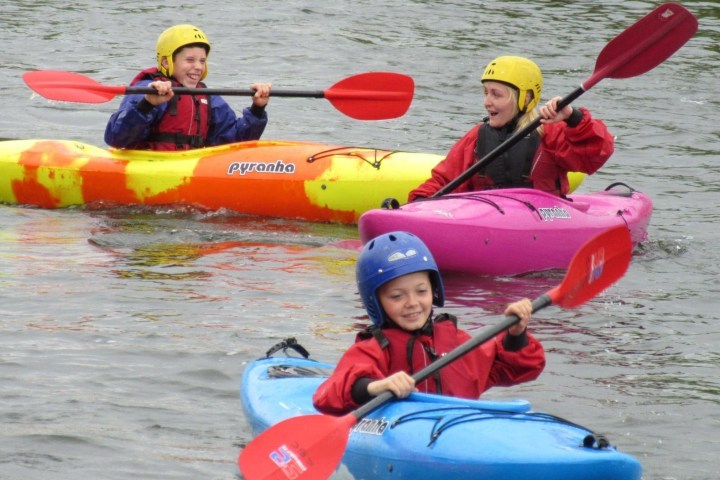 Three people in colorful kayaks paddling on a calm river.