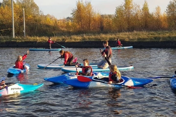 People kayaking on a calm river surrounded by autumn trees.
