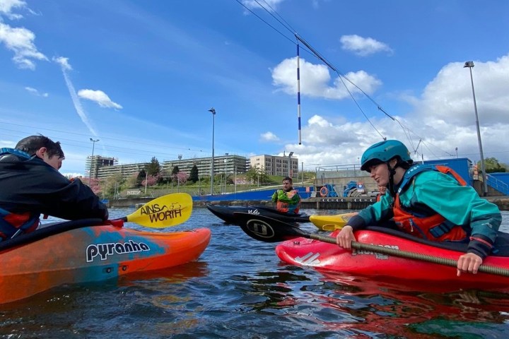 People kayaking on a sunny day with buildings in background.