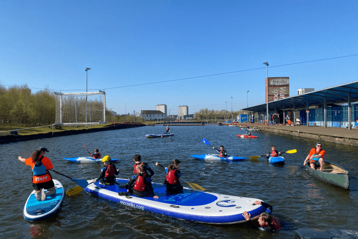 People kayaking and paddleboarding on a sunny day in a canal.