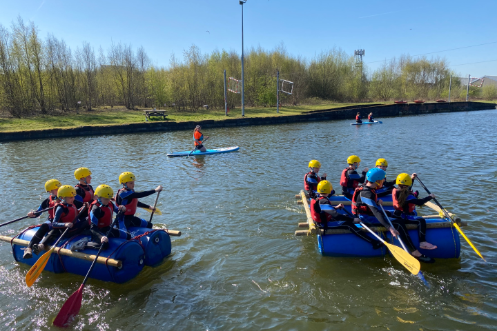 Groups rafting on a calm lake, wearing helmets and life vests under a clear blue sky.