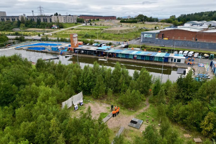 Overhead view of industrial area with trees, buildings, and people in orange jackets.