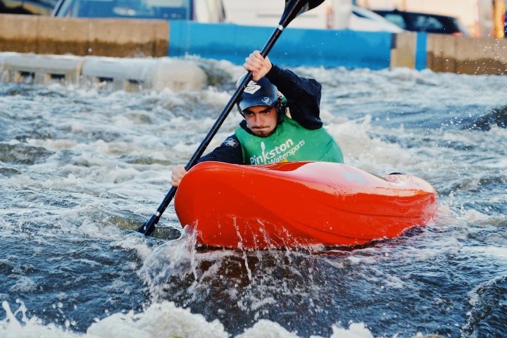 Person kayaking through rough water, wearing a green vest and blue helmet.