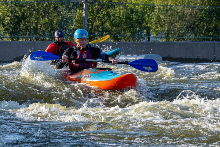 Two people kayaking through whitewater rapids, wearing helmets and life vests.