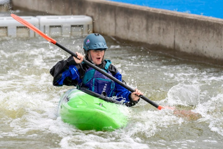 Person kayaking on whitewater rapids, wearing helmet and life jacket.