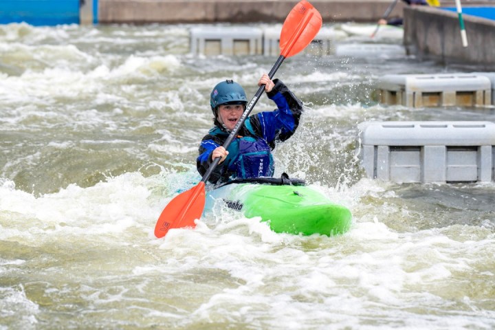 Person kayaking through rough water, holding a paddle and wearing a helmet.