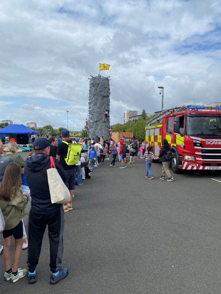 Crowd at outdoor event with climbing wall and fire truck nearby.