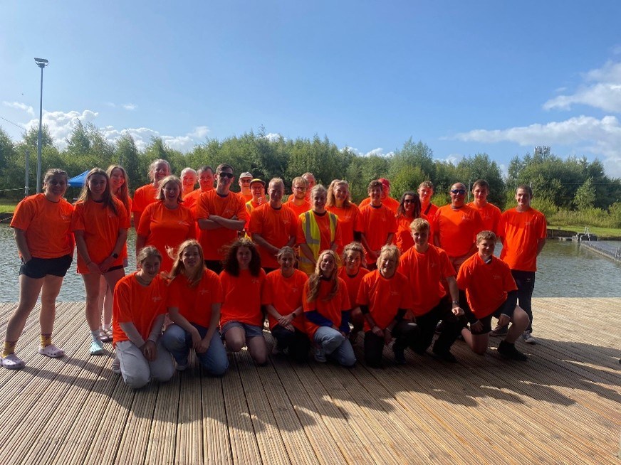 Group of people in orange shirts posing on a wooden deck near water.