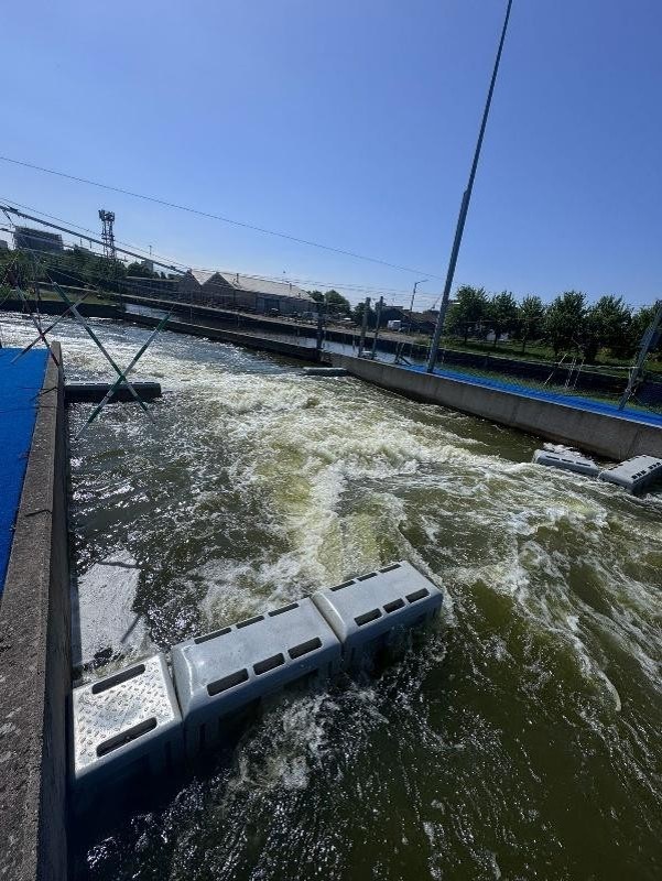 Outdoor water channel with artificial rapids under a clear blue sky.
