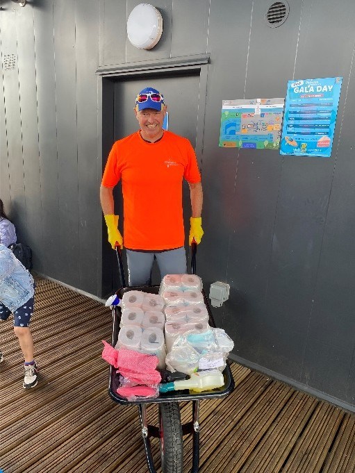Person in orange shirt with wheelbarrow full of cleaning supplies.